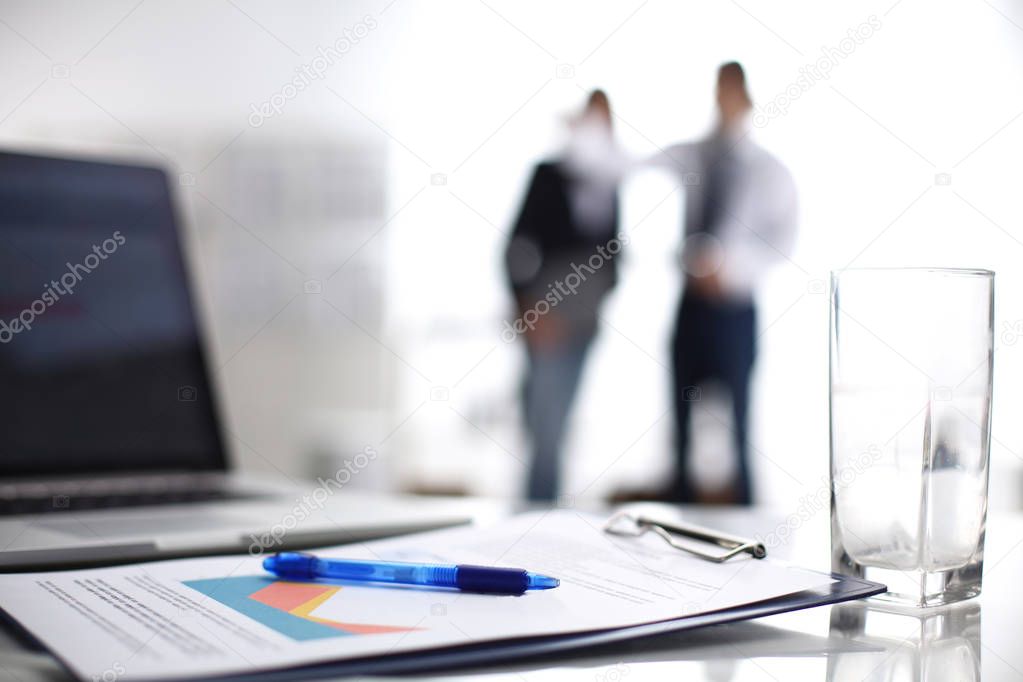 Laptop computer with folder on desk , two businesspeople standing in the background