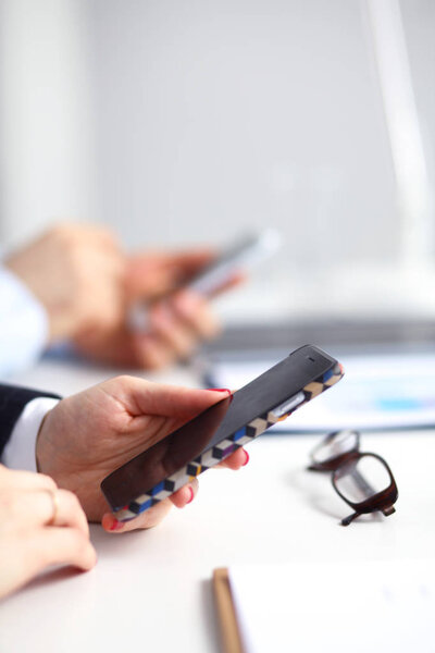 Businesswoman using her phone in office sitting on desk, selective focus