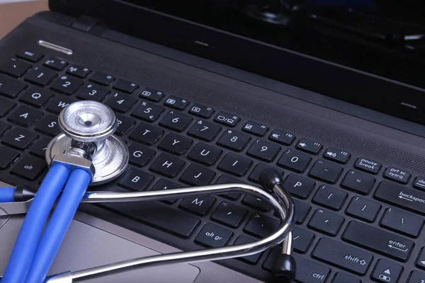 Uno stetoscopio medico vicino a un computer portatile su un tavolo di legno, su bianco — Foto Stock