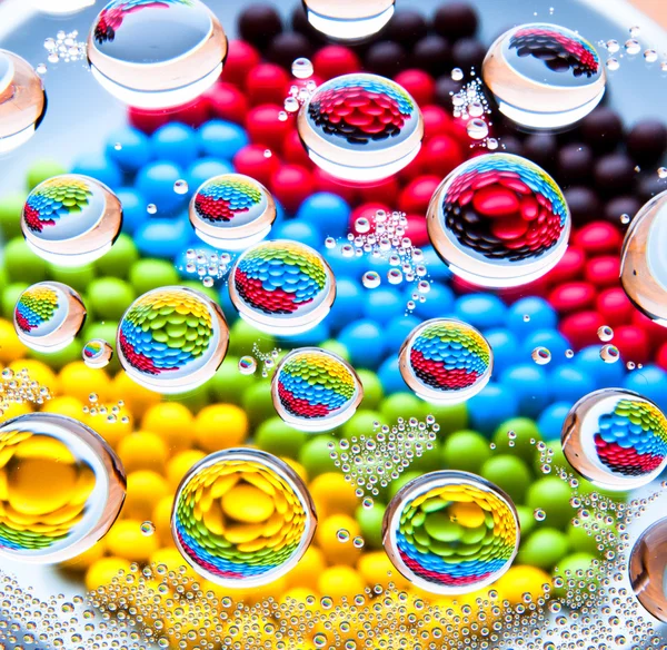 Gotas de agua sobre colorido arco iris de chocolate lentejas fondo — Foto de Stock