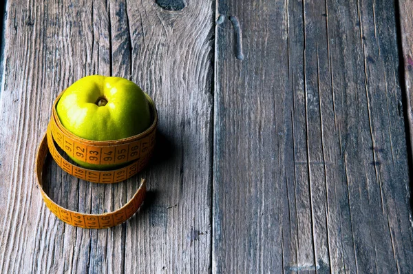 Grüner Apfel mit Maßband umwickelt Schneider. Holzuntergrund. Kopierraum — Stockfoto