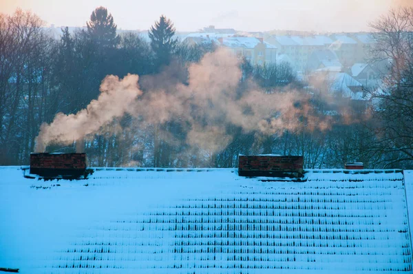 Techos cubiertos de nieve al amanecer. Humo de las chimeneas — Foto de Stock