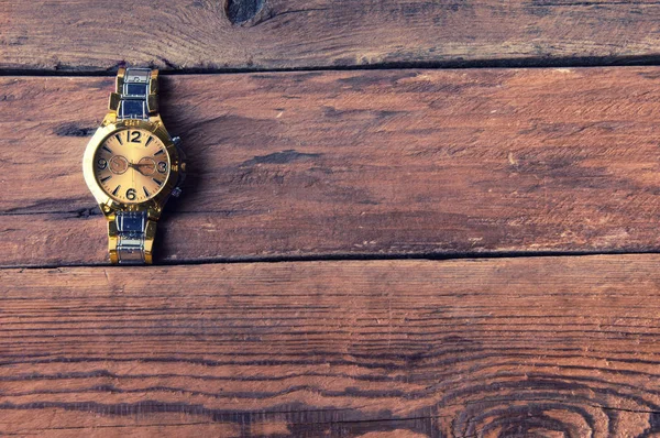 Golden hand watch on wooden table, copyspace
