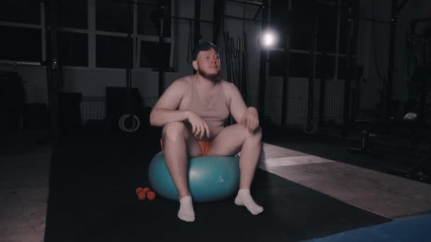 Fat guy yawns sitting on a ball in the gym — Stock Video