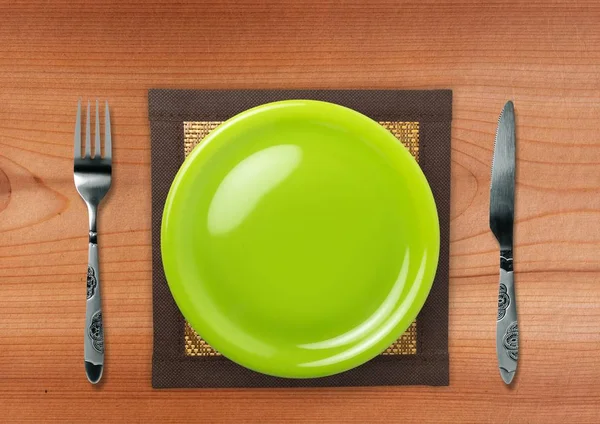 Ein Holztisch mit einem leeren grünen Teller. — Stockfoto