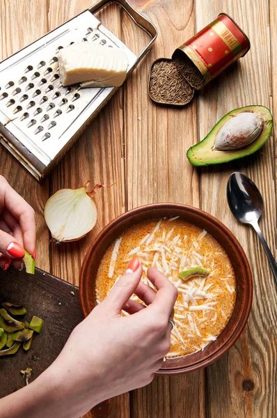 Женская рука кладет кусочки авокадо в кремовый суп. Процесс приготовления традиционного аргентинского картофельного супа Локро. Женщина-повар на кухне . — стоковое фото