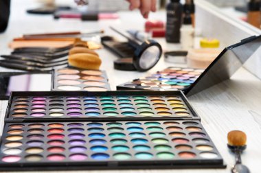 Birçok farklı kozmetik ve fırçalar salon bir tablo. Bir güzellik salonunda çalışıyorum. Renkli kozmetik ahşap çalışma alanı üzerinde. Göz farı, allık, toz, profesyonel kozmetik ve makyaj fırçaları. 