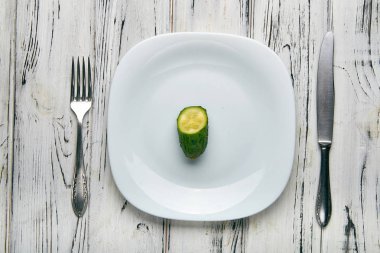Bir kız için sıkı bir diyete kadın yemek. İki küçük komik yeşil salatalık beyaz düz plaka üzerinde sivilce ile. Kilo vermek için çok az yiyecek. Kötü beslenme uzmanı tarafından Anti-obezite diyet.
