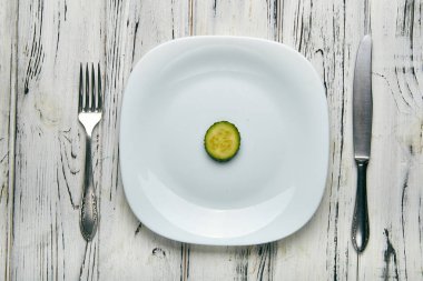 Bir kız için sıkı bir diyete kadın yemek. İki küçük komik yeşil salatalık beyaz düz plaka üzerinde sivilce ile. Kilo vermek için çok az yiyecek. Kötü beslenme uzmanı tarafından Anti-obezite diyet.