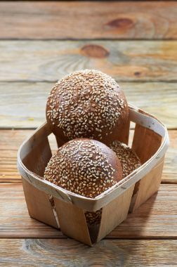 Susam alışılmadık bir sepet içinde ile karanlık hamur üç iştah açıcı buns. Dokuma ekmek sepeti vintage bir ahşap masa akşam yemeği için. Taze kokulu leziz ev yapımı hamur işleri.