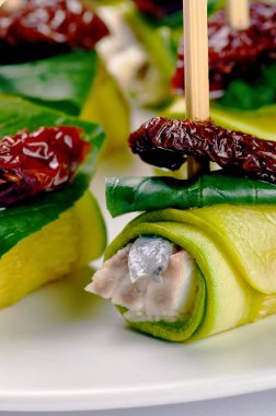 Olağandışı lezzetli meze Şef. Rulo ile beyaz balık, kabak, kurutulmuş domates, Kuru erik şiş üzerinde. Gıda Yeşiller, fesleğen, taze ıspanak yaprağı ile süslüdür.