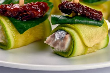 Olağandışı lezzetli meze Şef. Rulo ile beyaz balık, kabak, kurutulmuş domates, Kuru erik şiş üzerinde. Gıda Yeşiller, fesleğen, taze ıspanak yaprağı ile süslüdür.