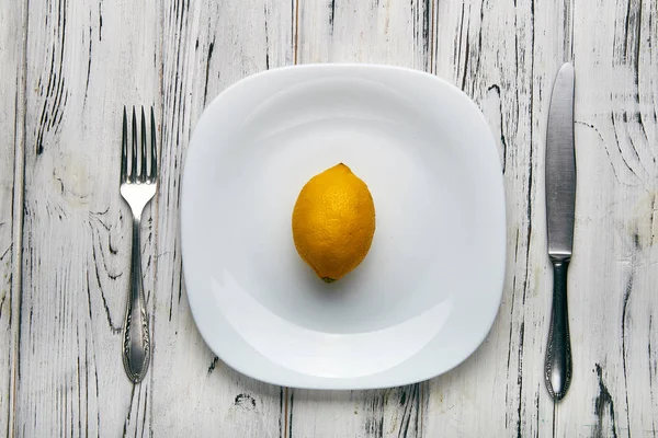 Ест для девушки, женщины на строгой диете. Ярко-желтый кислый лимон на белой тарелке. Слишком мало еды для похудения. Диета против ожирения от злого диетолога . — стоковое фото