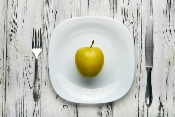 Ест для девушки, женщины на строгой диете. Большое сочное зеленое фермерское яблоко на белой тарелке. Слишком мало еды для похудения. Диета против ожирения от злого диетолога . — стоковое фото