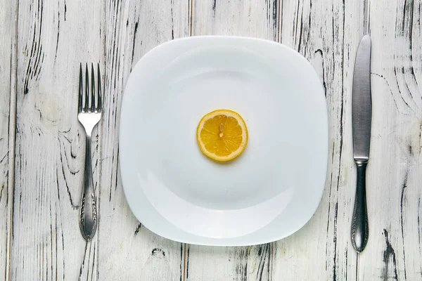 Spiser for en pige, kvinder på en streng diæt. Bright gul sur citron på en hvid almindelig plade. For lidt mad til at tabe sig. Anti-fedme kost af onde ernæringsekspert . - Stock-foto
