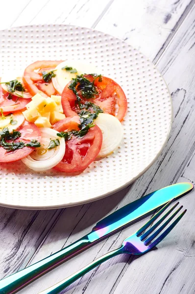 Güzel bahar salata domates, soğan, peynir ve yeşil giyinme. Büyük zarif tabağa yemek. Olağandışı yanardöner çatal bıçak takımı. Bir beslenme uzmanı sağlıklı bir diyet için lezzetli ve kolay yemek.