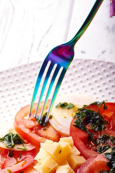 Güzel bahar salata domates, soğan, peynir ve yeşil giyinme. Büyük zarif tabağa yemek. Olağandışı yanardöner çatal bıçak takımı. Bir beslenme uzmanı sağlıklı bir diyet için lezzetli ve kolay yemek.