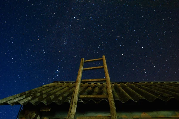 Aldeia. Velha escada de madeira apoiada contra o celeiro com um telhado de ardósia no céu estrela da noite. A escadaria leva ao céu . — Fotografia de Stock