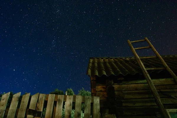 Village. Vieille échelle en bois appuyée contre la grange avec un toit en ardoise dans le ciel étoilé nocturne. L'escalier mène au ciel . — Photo