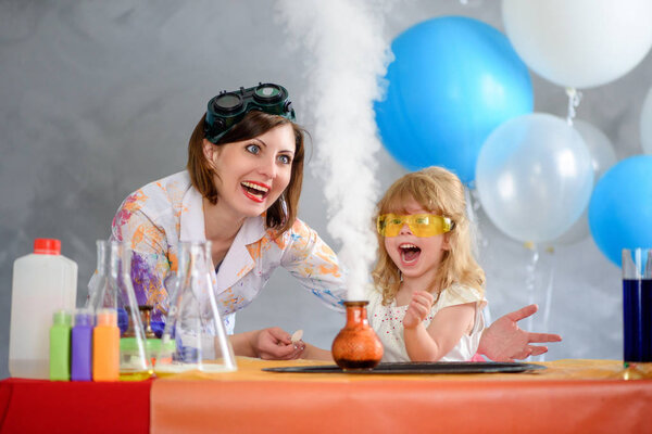 Crazy professor woman conducting chemical experiments in the company of a little smiling girl.