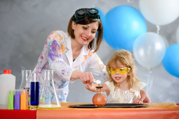 Crazy professor woman conducting chemical experiments in the company of a little smiling girl.