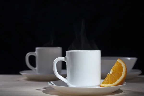 Белая кружка с паром из чая рядом с ломтиком апельсина — стоковое фото