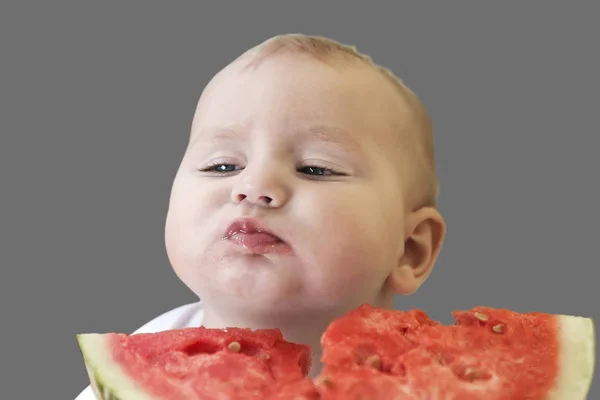 Bebê ativo adorável é muito saboroso comer uma melancia, isolar em um fundo cinza . — Fotografia de Stock