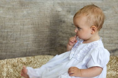 Parmağını ağzına tutarak halı üzerinde oturan küçük şirin kız.