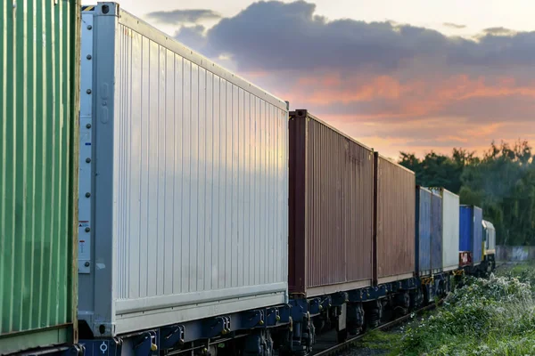 I container ferroviari multicolori vanno all'orizzonte per ferrovia verso un bellissimo tramonto — Foto Stock