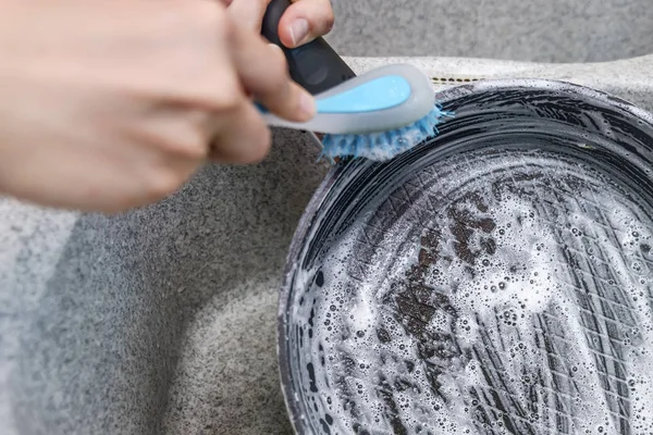 woman launches a burnt pan with a blue brush in the kitchen sink.