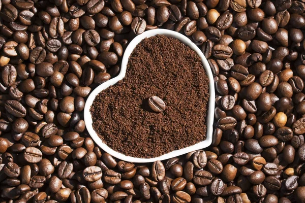 Grain of roasted coffee in a cup in the form of a heart in a pile of coffee beans, background