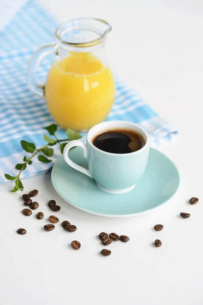 Strong black coffee in a light blue cup on a white table with orange juice