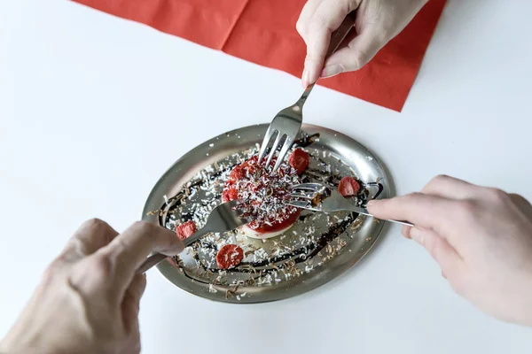 Three hands with three dessert forks stretch to a small strawber