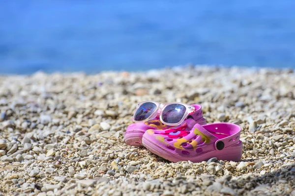 Pink beach kid's crocs / sandals and sunglasses on sandy beach. Royalty Free Stock Photos