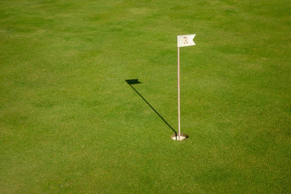 Glof flag mark in hole throwing shadow on the green course grass Stock Image