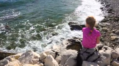Küçük kız sahilde oturup oynarken kayalar