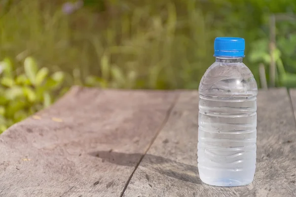 Plastic water bottle on wooden table texture with nature.