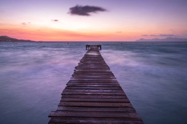 Mayorka Puerto de Alcudia sahil iskelesi güneş doğarken İspanya 'nın Mallorca Balearic adalarındaki Alcudia körfezinde renkli bulutlu manzarayla