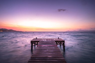 Mayorka Puerto de Alcudia sahil iskelesi güneş doğarken İspanya 'nın Mallorca Balearic adalarındaki Alcudia körfezinde renkli bulutlu manzarayla