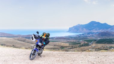 Motorsiklet ve deniz kıyısındaki bir dağda kamp malzemeleri.