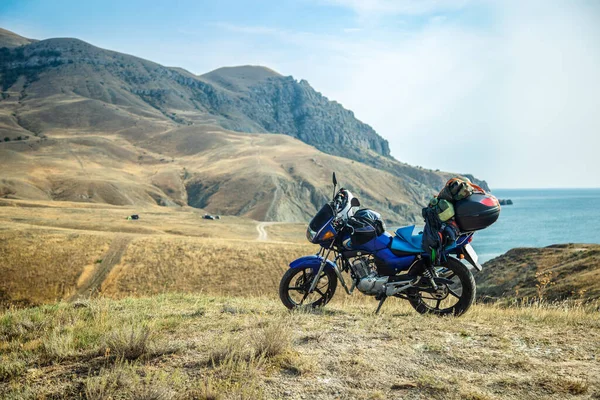 Motorsiklet ve deniz kıyısındaki bir dağda kamp malzemeleri.