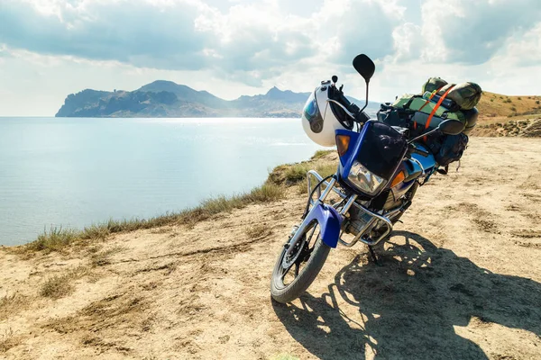 Motorsiklet ve deniz kıyısındaki bir dağda kamp malzemeleri.