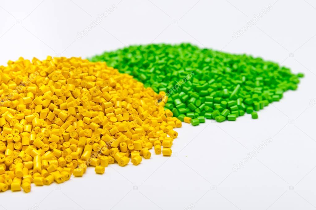 Green and yellow plastic pellets on a white background. Polymeri