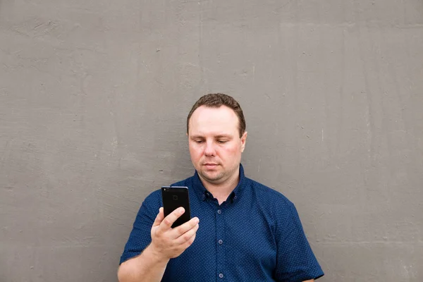 Den unge mannen i den blå tröjan använder sin smarta telefon stående av — Stockfoto