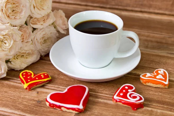 Der Hintergrund des Valentinstages. Tasse Kaffee, Blumen, Lebkuchenherz auf Holzgrund — Stockfoto