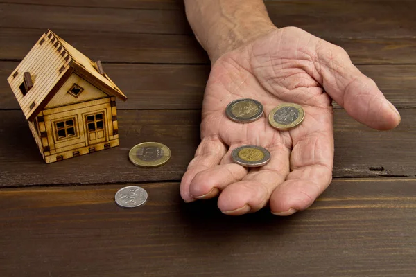 Starzec ręce i model domu z monet na stole. The — Zdjęcie stockowe