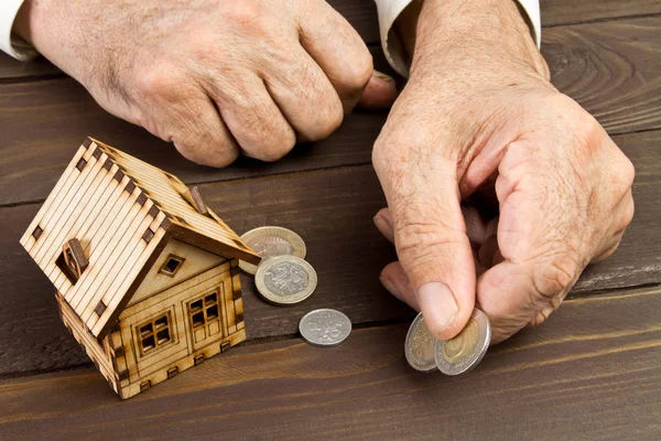 Old man hands and a model home with the coins on the table .The