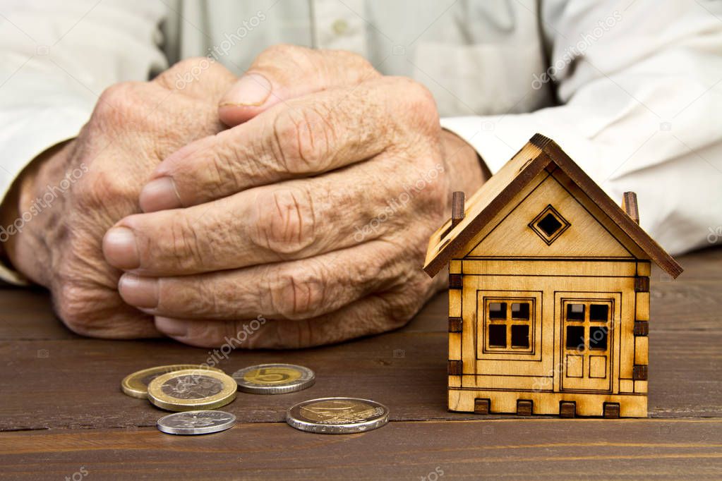 Old man hands and a model home with the coins on the table .The 