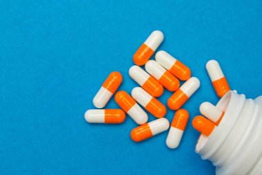 Orange white capsules (pills) were poured from a white bottle on clipart