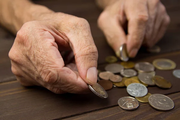 Ręce żebrak z kilka monet. Pojęcie ubóstwa. Osoby w podeszłym wieku na Pensjonat posiada monety na tle drewniany stół — Zdjęcie stockowe